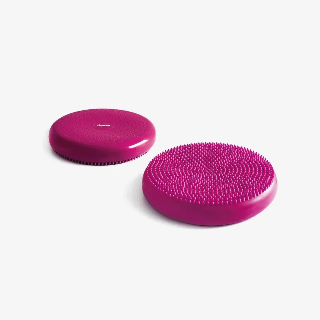 Zwei runde, lilafarbene Balancekissen auf weißem Hintergrund; ein Kissen hat eine glatte, strukturierte Oberfläche, während das andere kleine, erhabene Unebenheiten für Grip und Stimulation aufweist.
